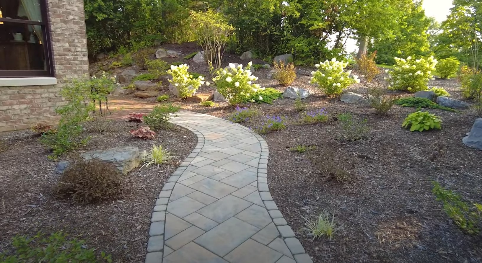 Curved stone pathway through professionally landscaped garden with flowering shrubs and mulched beds