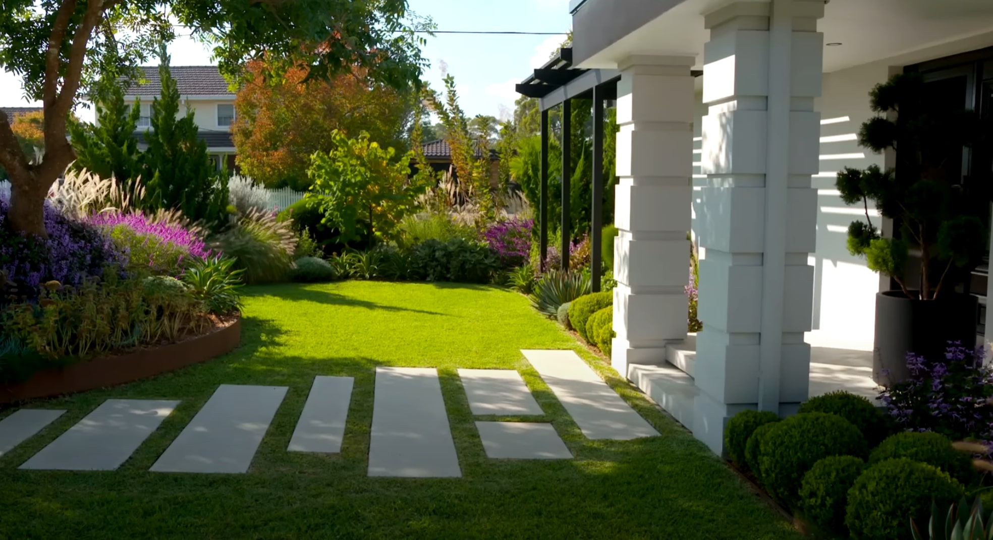 Modern residential front yard with geometric concrete pavers, vibrant flower beds, and professional landscape design
