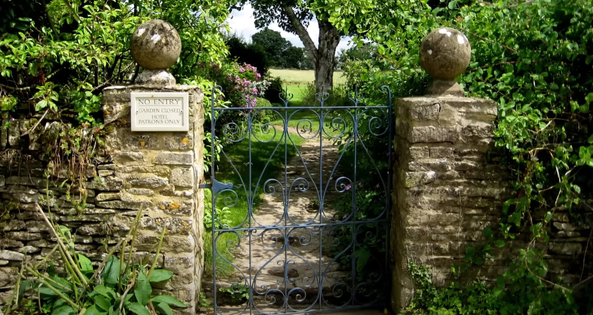 Traditional stone garden entrance with decorative iron gate and established landscape plantings Vintage stone garden gate entrance with decorative ironwork and mature landscaping